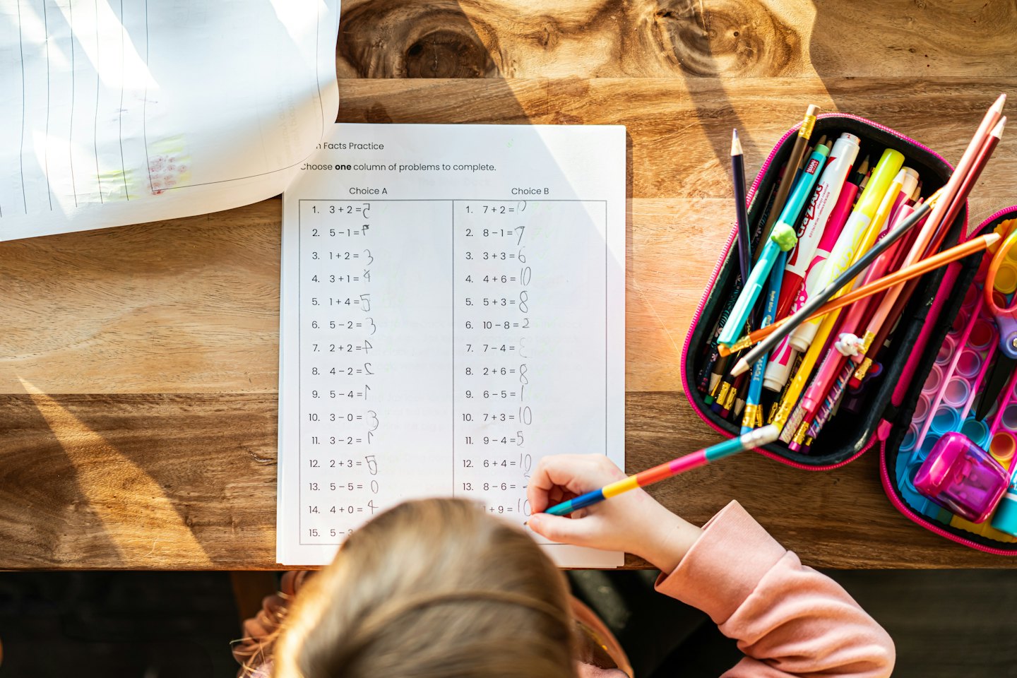 Dziecko rozwiązuje kartkówkę z matematyki przy drewnianym biurku.