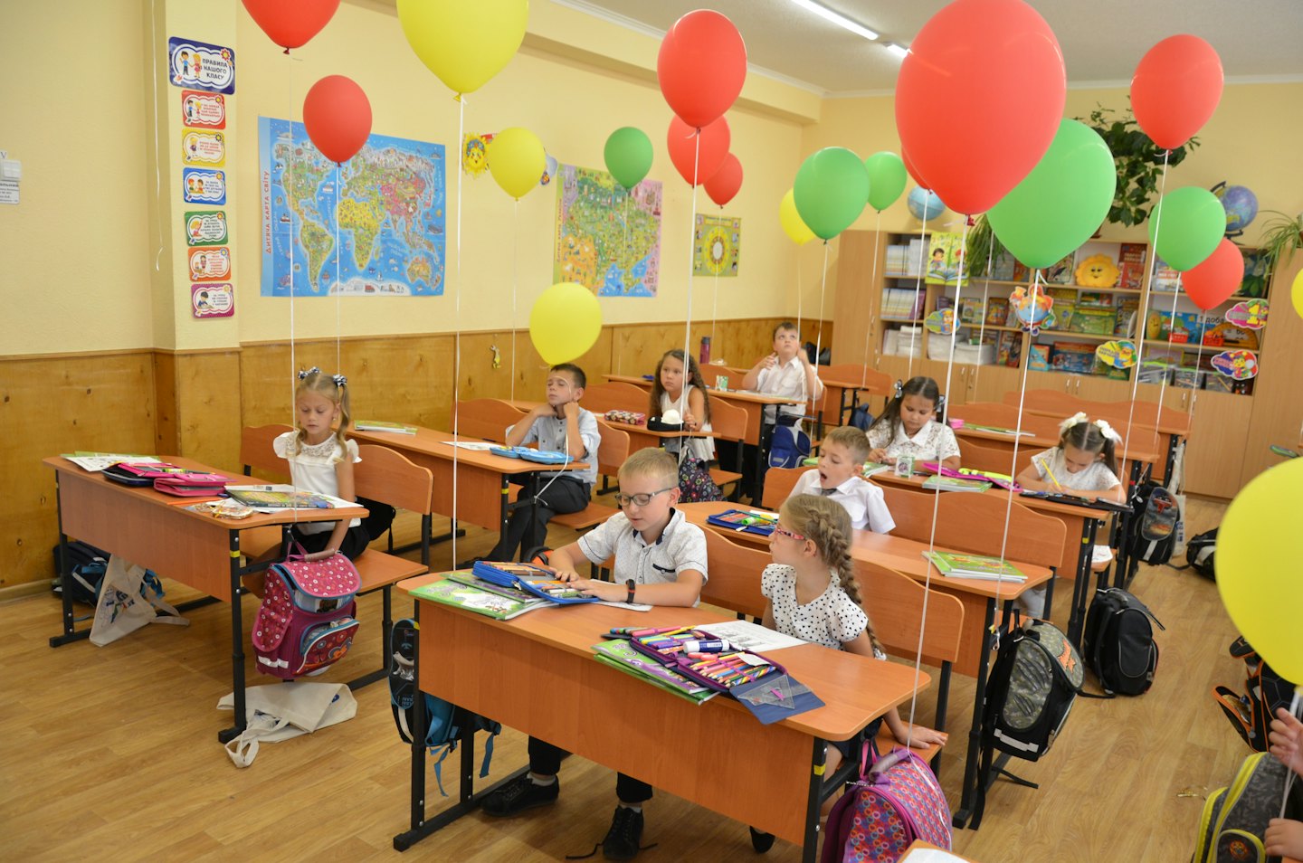 Dzieci siedzą przy drewnianych ławkach w udekorowanej sali lekcyjnej.